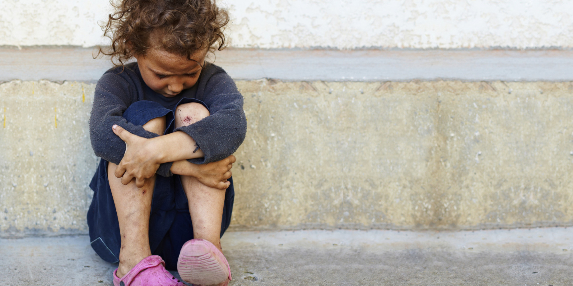 poor, sad little child girl sitting against the concrete wall